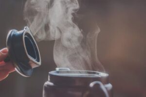 Close-up of steam rising from an open container lid showing hot liquid.